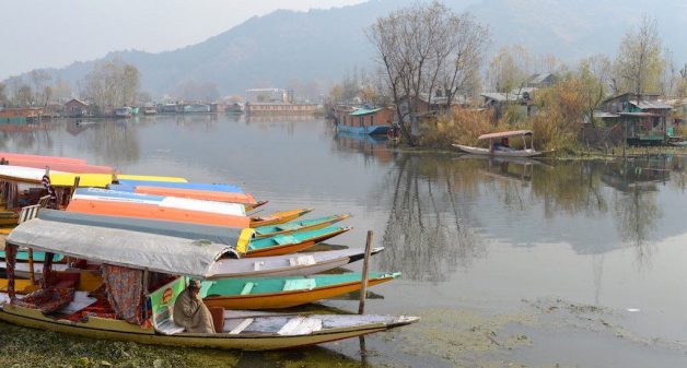 A boatman in Dal Lake warms himself with a fire pot under his pheran cloak. Credit: Athar Parvaiz